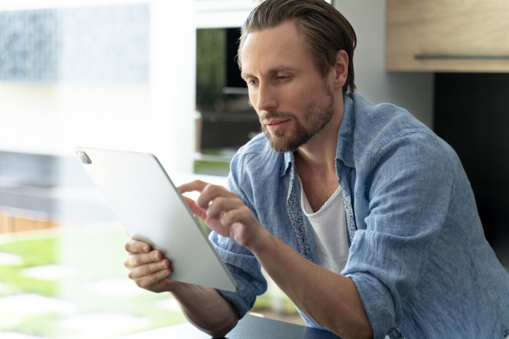 Man using a tablet at home, looking concerned while checking something online.