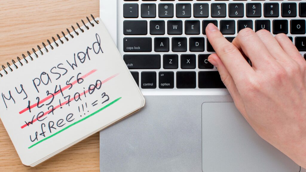 A notebook with handwritten passwords beside a laptop keyboard, symbolizing simple steps anyone can take to protect their online accounts.