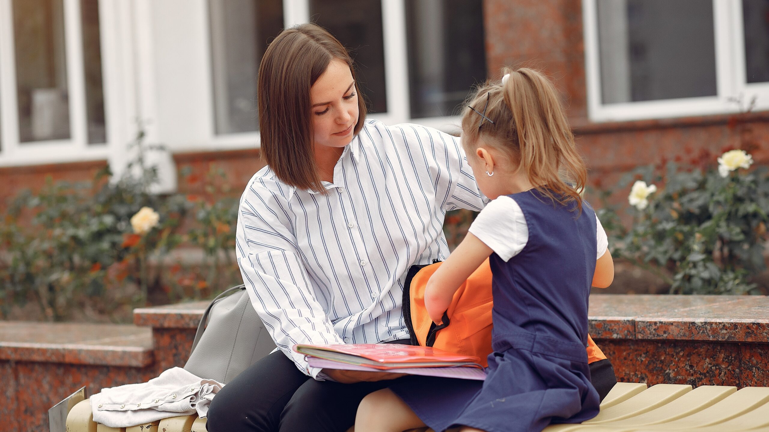 Mother helping her daughter pack a school backpack outdoors