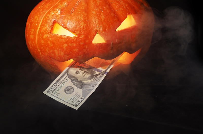 Carved pumpkin gripping a $100 bill — symbol of Halloween shopping scams