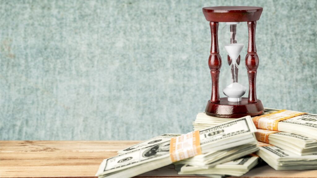 Hourglass on stacks of cash, symbolizing how timeless scams are in our lives.