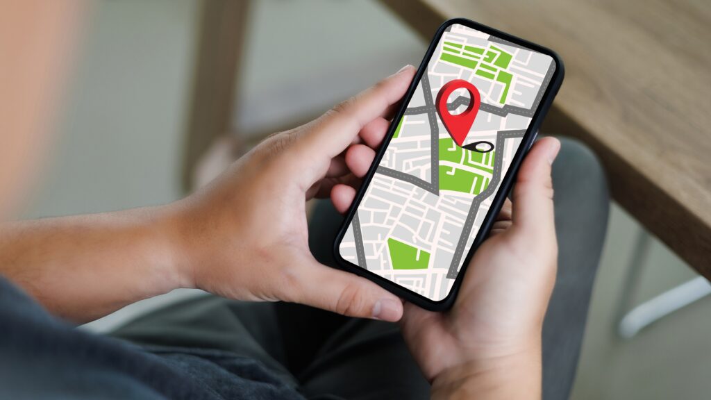 Person holding a smartphone showing a map with a large red location pin, symbolizing how apps track and share your movements.