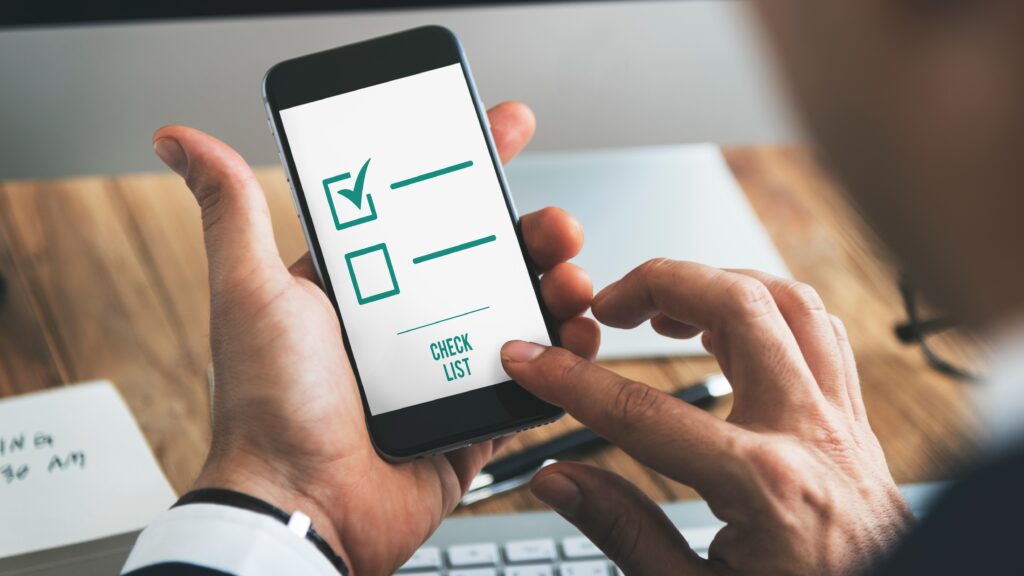 Close-up of a person holding a smartphone with a simple checklist on the screen, marking an item as completed.
