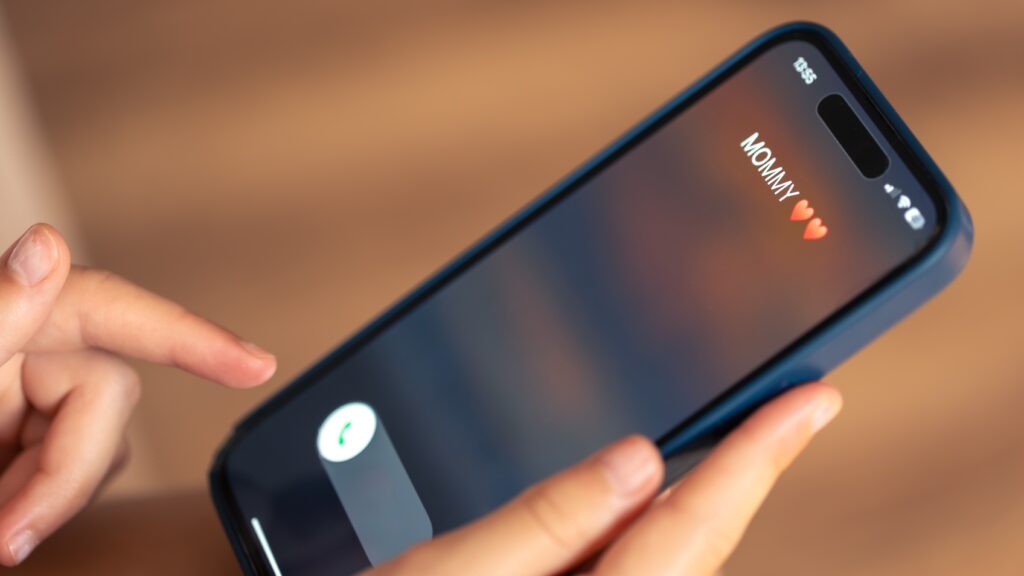 Person holding a phone showing a "Mommy” caller, symbolizing AI-generated voice scams that mimic family members to demand urgent money.