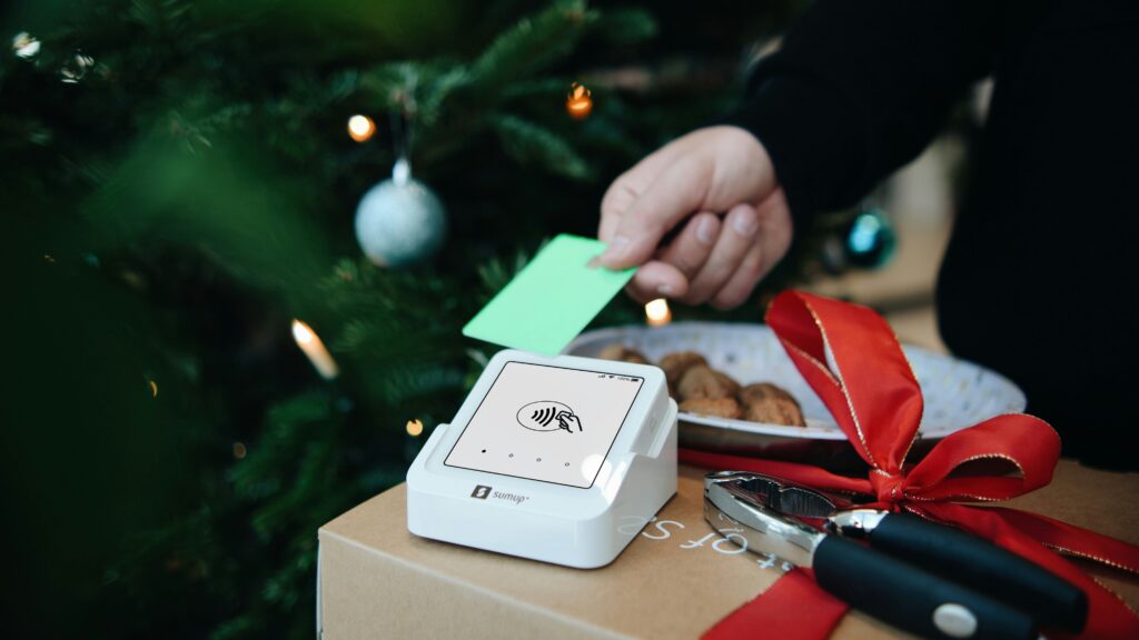 Close-up of a person using a credit card on a contactless payment terminal near Christmas decorations, symbolizing safe holiday shopping and secure payments.