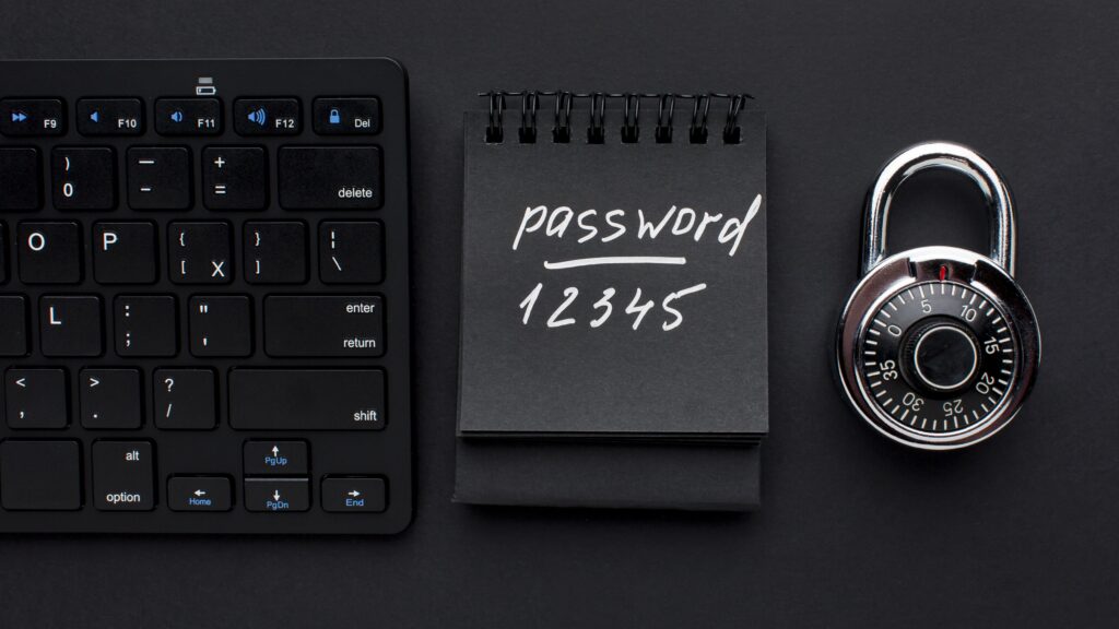 A notepad with “password 12345” written next to a computer keyboard and lock, represents weak passwords and the illusion of safety they give.