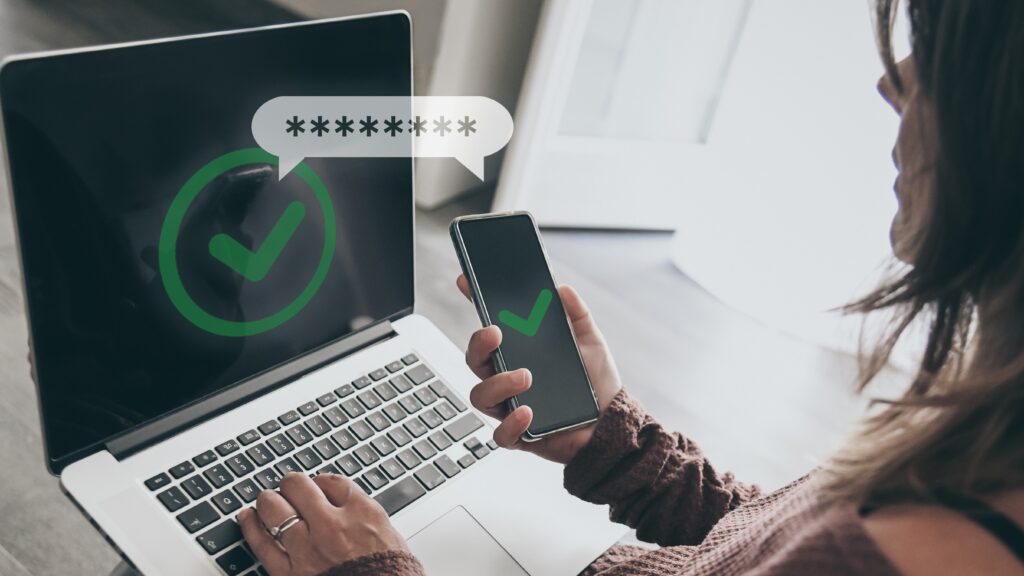 A woman holding a smartphone while a laptop screen shows a green verification checkmark — symbolizes secure habits and second-step verification.