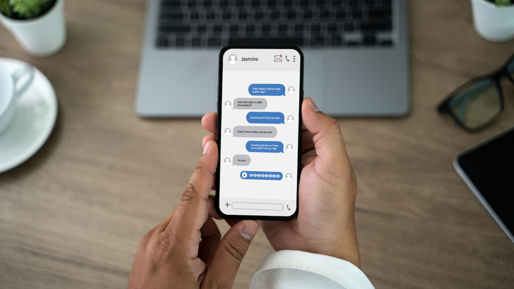 Person holding a smartphone and reading a private chat message on a desk with a laptop nearby.