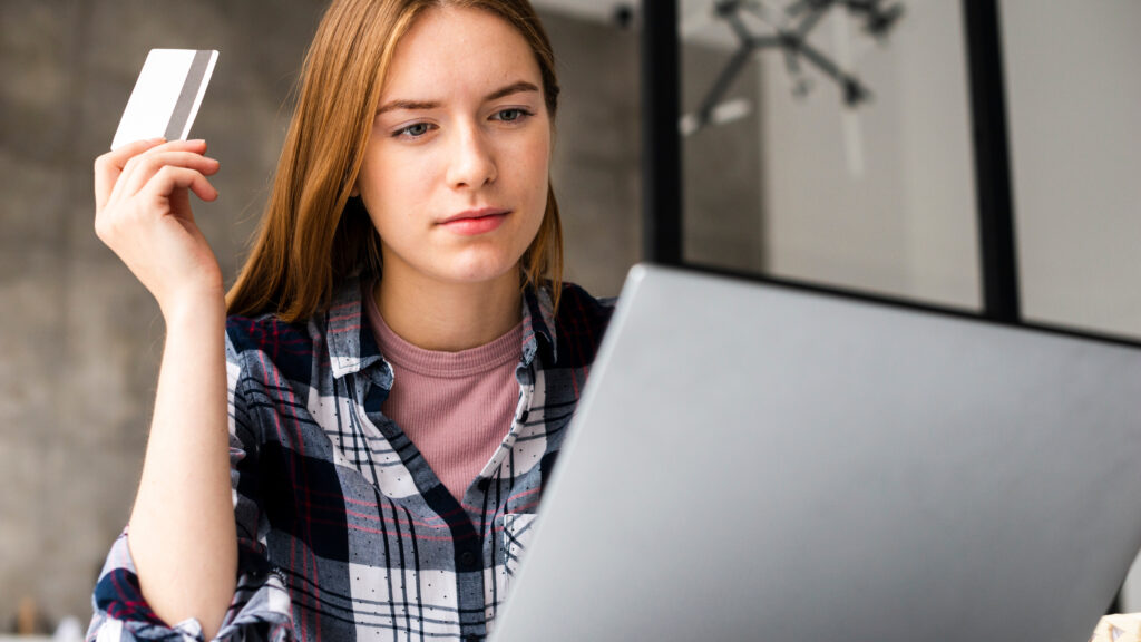 A woman holding a credit card and looking at a laptop, illustrating safe online banking practices during Awareness Week.