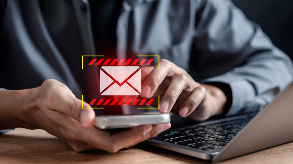 Person holding a smartphone with a warning icon over an email message, representing phishing and scam emails.