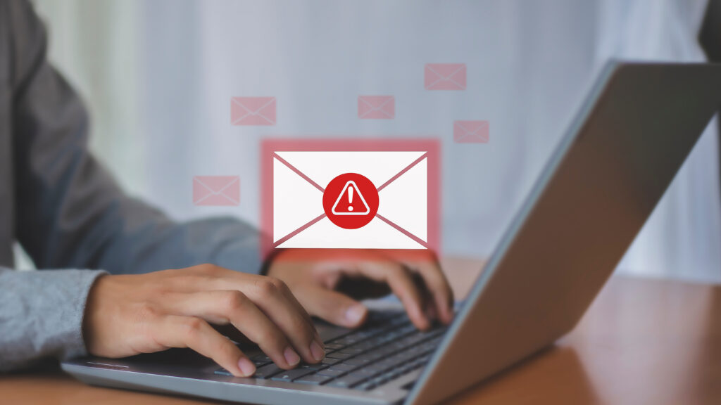 Person typing on a laptop with a warning icon over an email, representing fake government alerts and scam messages.