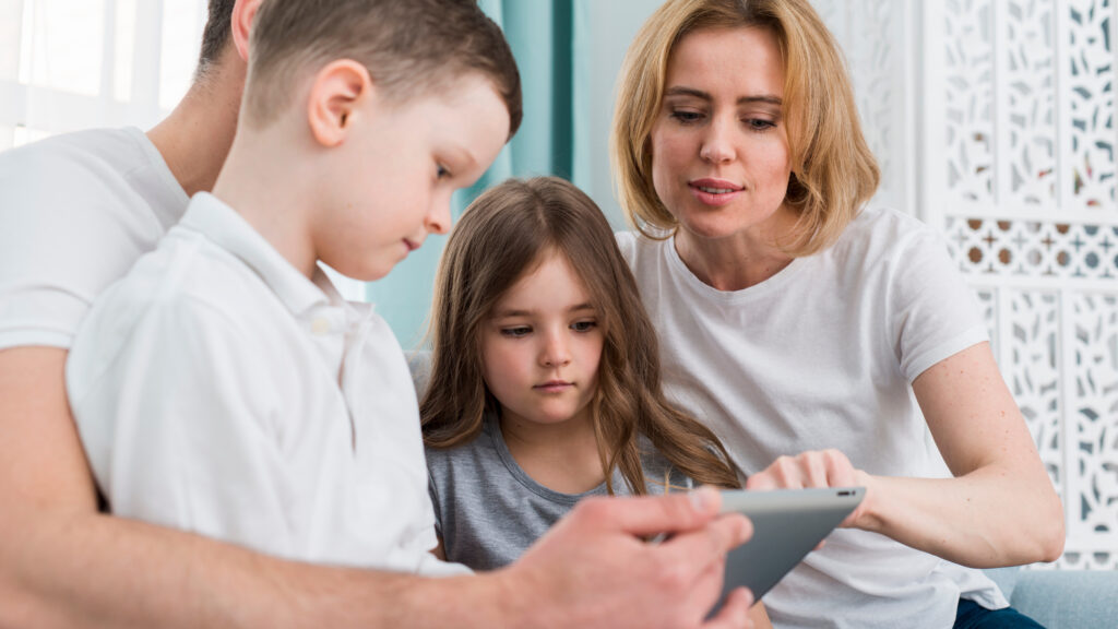 Parent explaining online safety to children while reviewing a message together on a tablet