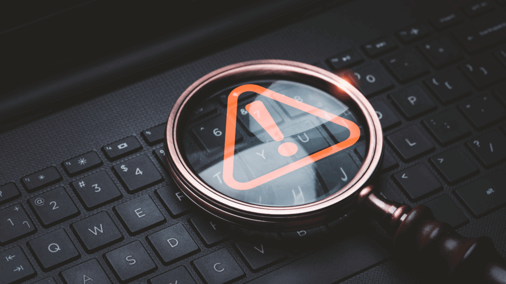 A magnifying glass highlights a warning symbol on a laptop keyboard, representing data breach risks