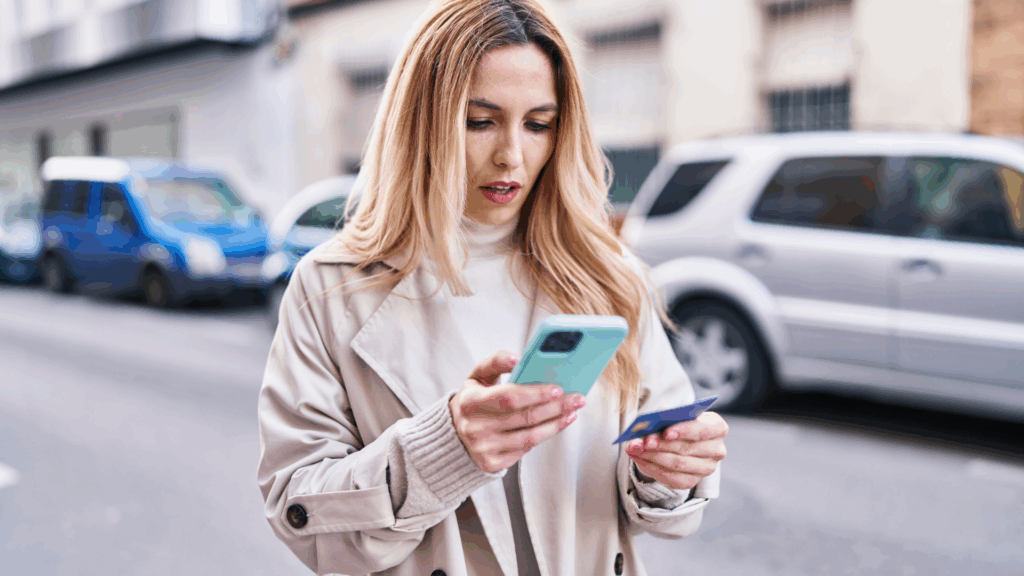 Woman checking a toll payment message on her phone while holding a credit card, illustrating a potential E-ZPass text scam.
