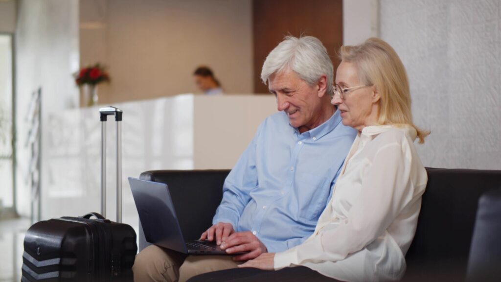 Older couple using a laptop at a hotel lobby with luggage