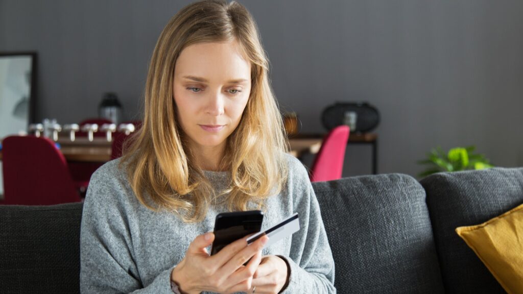 Woman looking at her phone while holding a credit card