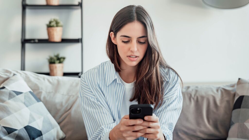 Woman looking at her smartphone, reviewing social media content at home