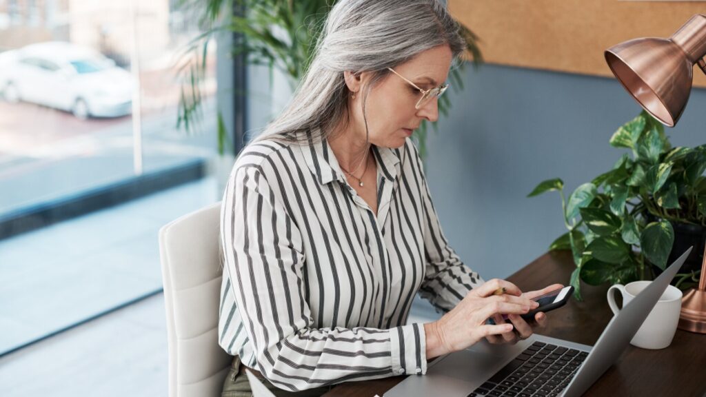 Woman checking a suspicious message on her phone about an Apple account while using a laptop