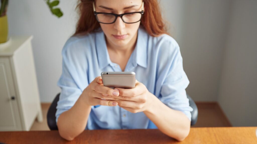 Woman looking closely at her smartphone after searching online for customer support, illustrating how scammers can trick people through fake phone numbers in search results.
