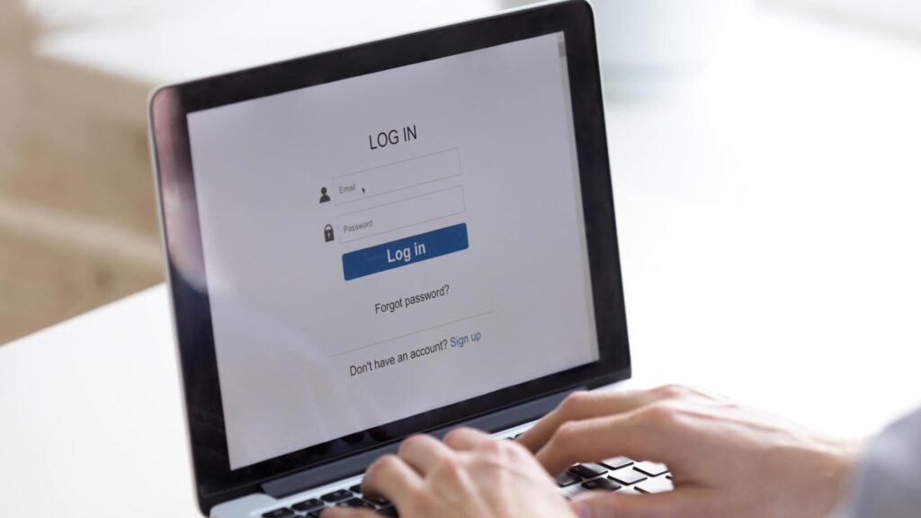 Person signing into an online account on a laptop, illustrating the importance of updating weak or compromised passwords to improve account security.