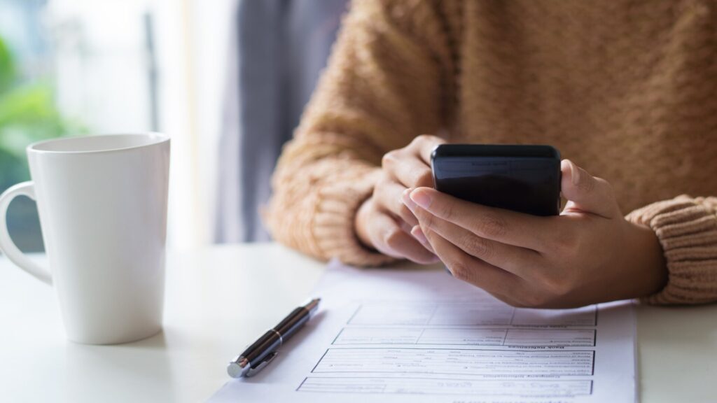 Person checking a phone beside paperwork, illustrating steps to monitor financial activity and suspicious messages after a data breach.