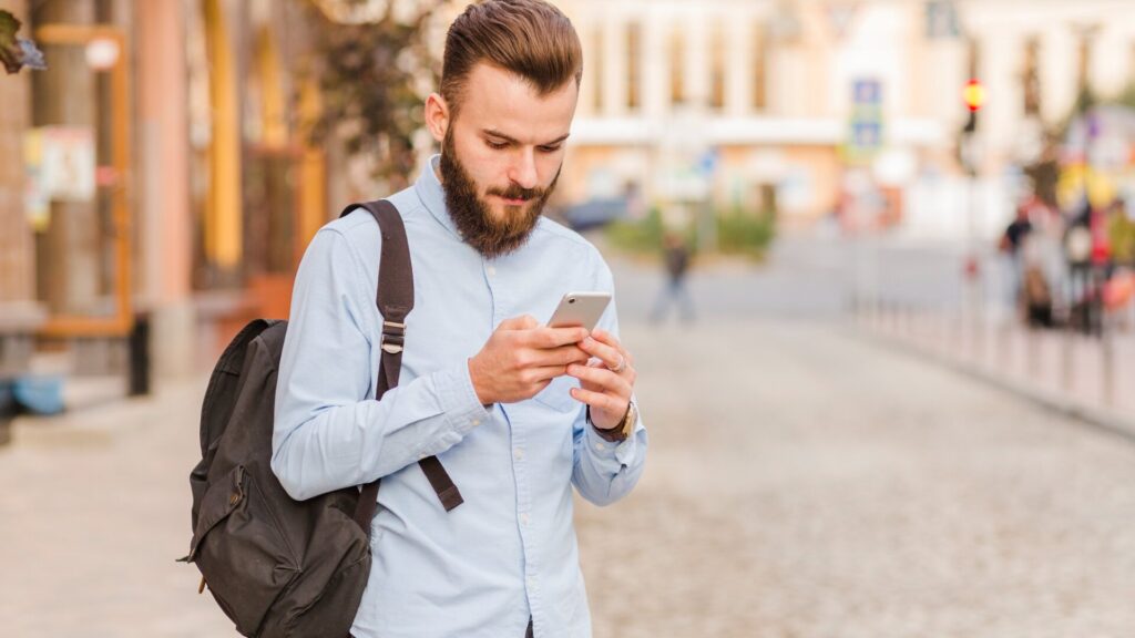 Traveler checks a smartphone near a train station, illustrating steps to avoid scams after the Trenitalia data breach.