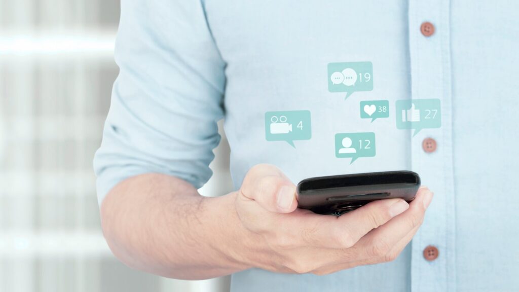 A person checks a smartphone with digital notification icons representing messages, account activity, and online alerts.