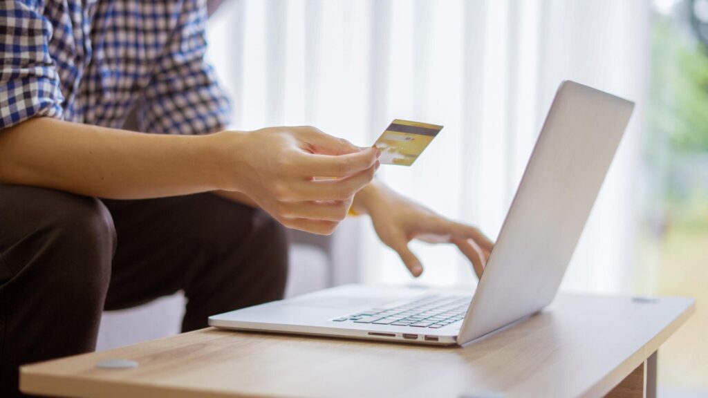 Person using a credit card on a laptop, representing fake hotel payment requests sent after a data breach.
