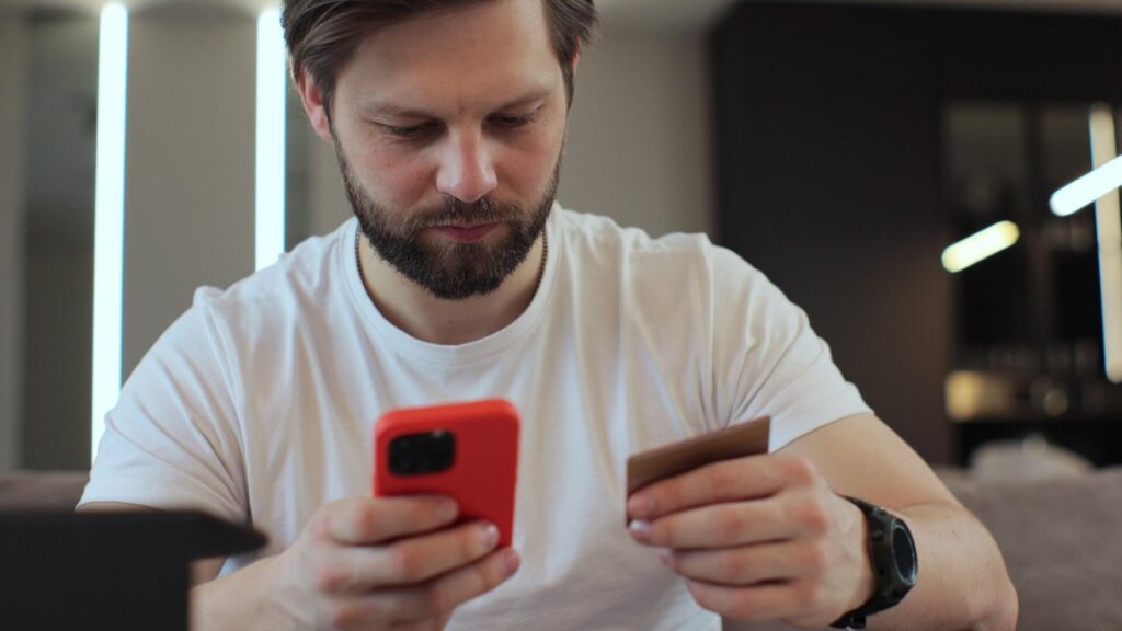 Man using a smartphone and bank card as he manages an online account and considers safer ways to protect his email privacy.
