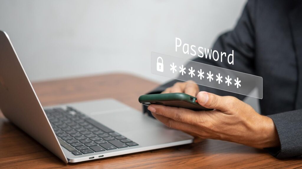 Person using a smartphone next to a laptop with a password login screen, representing account security and protection against FIFA phishing scams.