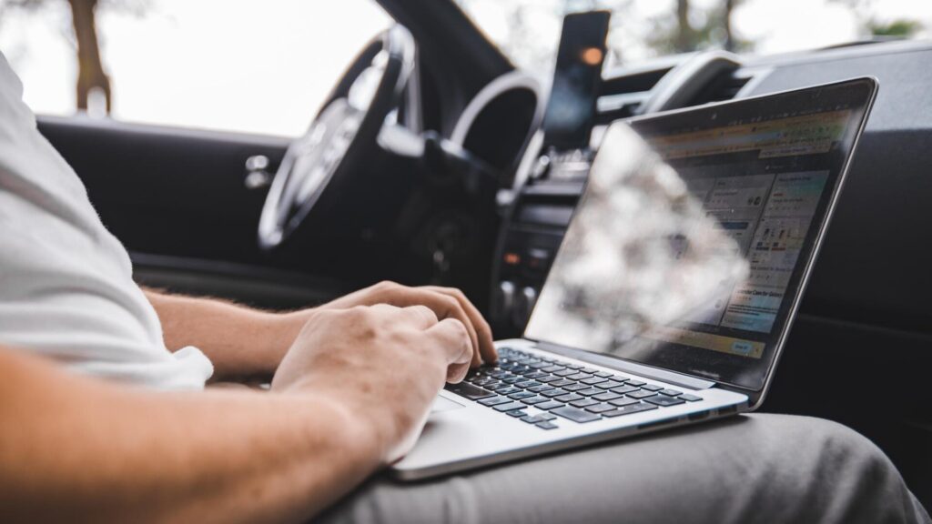 Person using a laptop inside a car, representing online privacy checks after Flock license plate search data was leaked.