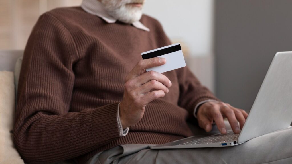Older man holding a credit card while using a laptop to check his financial accounts after a data leak.