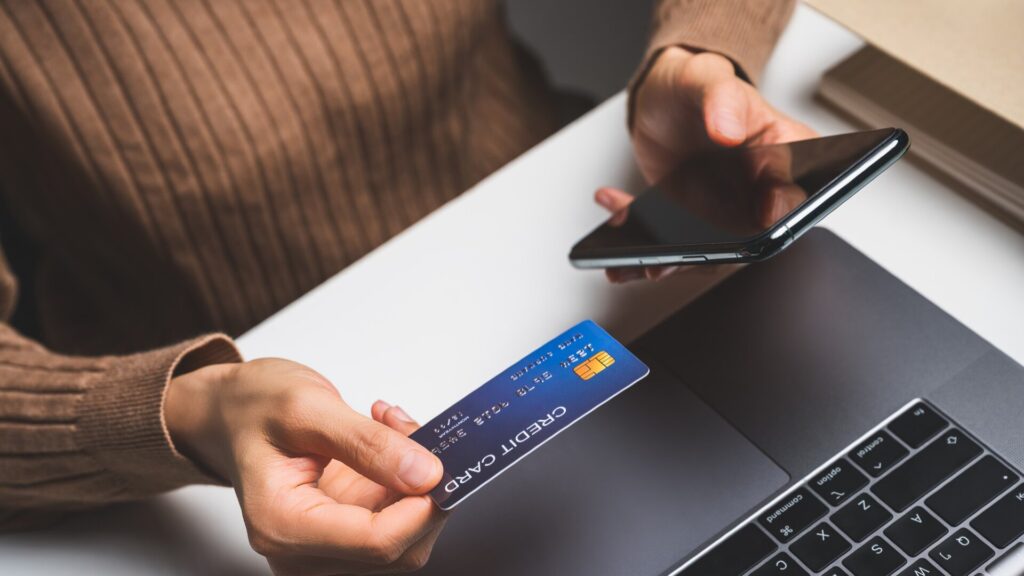 Person holding a credit card and smartphone while checking an online payment request.