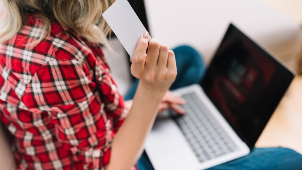 Woman holding a bank card while using a laptop to review her checking account and online payments.