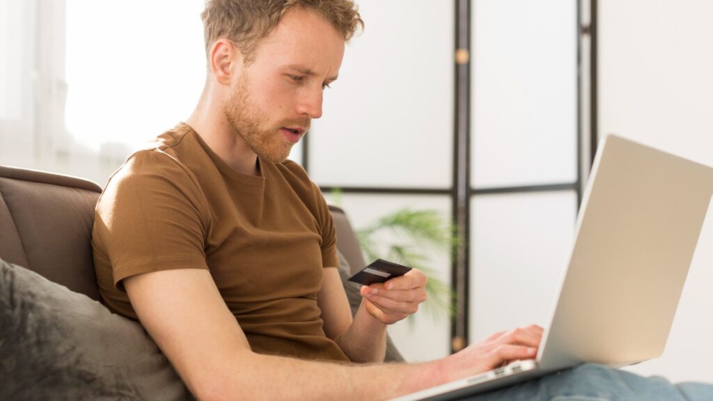 Man holding a payment card while using a laptop, representing identity theft and phishing risks after the Medtronic data breach.