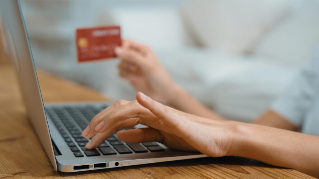 Person using a laptop while holding a credit card, representing financial checks after the AssuranceAmerica data breach.